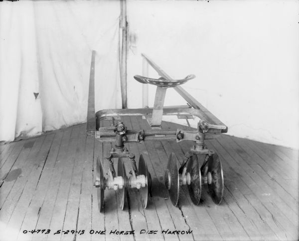 One Horse Disk Harrow set up on a wood floor with a cloth backdrop behind.