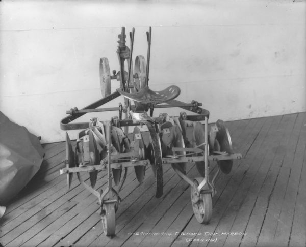 Orchard Horse Disk Harrow set up on a wood floor with a cloth backdrop behind. (Decn 1161).