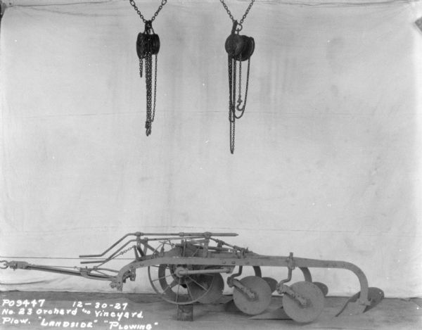 No. 23 Orchard and Vineyard Plow, Landside, Plowing, set up indoors on factory floor. A backdrop is behind the plow, and two pulleys with chains are hanging above.