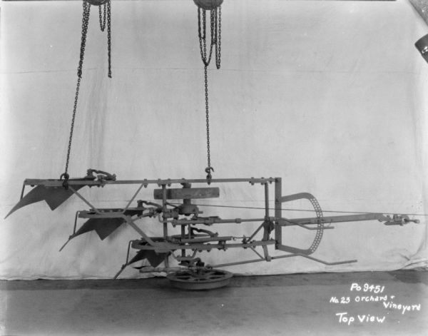 No. 23 Orchard and Vineyard. A backdrop is behind the plow, and two pulleys with chains are suspending the plow to show a top view.