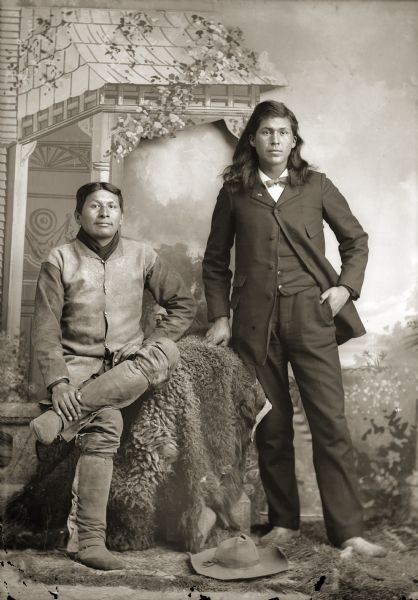 Full-length studio portrait of George Frank Buffalohead (WaChoZhoNoZheeKah), sitting on a prop stone wall, and Sam Carley Blowsnake (HoChunkHaTeKah). Sam was the subject of Paul Radin’s 1920 book, "Autobiography of a Winnebago Indian."