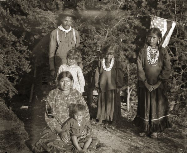 John Mike Jr. (HayShooKeekah), rear left, pictured with his family. Standing from left to right are daughters Ada Mike (HunkEWinKah), Lizzie Mike (WeHunKah), and Belle (Mattie) Mike (ENooKah). Wife Kate Mike (ENooKeeKah) is sitting with son Dewey Mike (WaHoPinNeKeKah) in her lap. Dewey Mike, who became an army private, was killed in action on August 30, 1918, in France. A member of Company A, 128th Infantry, he was among the twelve thousand Native Americans on active duty during World War I. At the time, most Native Americans were not United States citizens and were not granted citizenship until the passage of the Indian Citizenship Act of 1924. Dewey was honored posthumously in May of 1933 when his mother visited his grave. Kate Mike was the only Native American Gold Star Mother to be invited by the government to visit France. She made the trip despite her limited ability to speak English, laying a wreath of pine boughs from the trees Dewey played beneath when he was a boy on his grave.