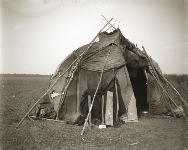The Ho-Chunk used many different materials to cover their lodges. The earlier lodges had coverings made of cattail mats, deer hides, and sheets of bark. This one is covered with canvas, with a smoke hole visible at the top. When residents were not home, they would simply allow a blanket or mat to hang down over the door opening. A stick or board leaned against the door would indicate that no one was home.