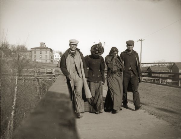 Four Ho-Chunk people crossing a bridge spanning the Black River. This photograph was taken before the flood of October 1911, when the bridge was completely destroyed.
