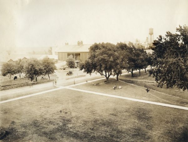 Elevated view of Poor Farm on the grounds of the Winnebago County Asylum. There is a large barn, silo, windmill, and the roof of a large building in the background.