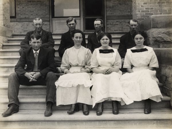 Group portrait of Winnebago County Asylum staff members sitting on steps, including the Superintendent, E.E. Manuel, seated in the back row, far right. George V. Grueder, seated on the left in the front row, was the Superintendent of the Asylum from 1930 to 1942.