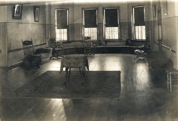 Interior view of a room, perhaps a lounge or common room, in the Winnebago County Asylum. There is a long window seat along the bay windows in the background.