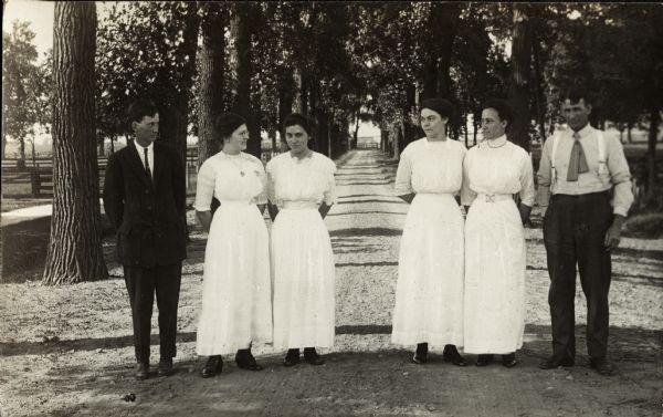 Four women and two men are standing at the tree-lined drive surrounded by a lawn which leads into the Winnebago County Asylum.  The man on far right in the group is George V. Grueder who later became the Asylum's superintendent; he served from 1930-1942. In this image he is a staff person.
