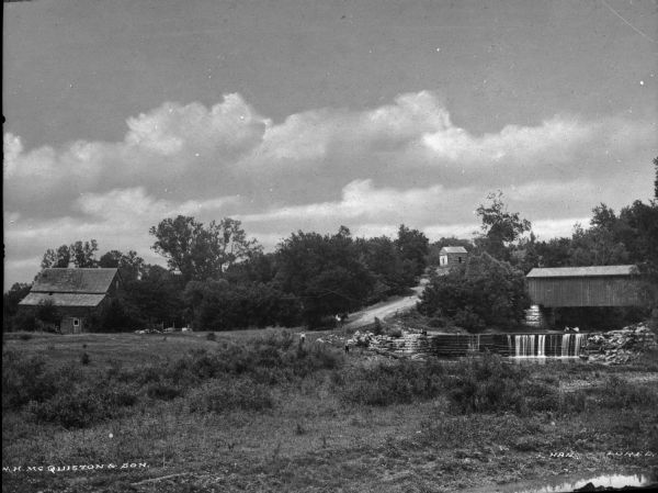 View of a country farmhouse and rural road. A covered bridge and dam can be seen nearby. Text on photograph reads: "N.H. McQuiston & Son."
