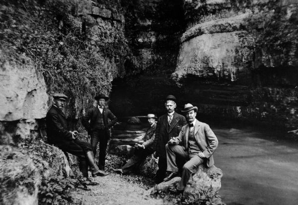 Five men in suits pose near the Roaring River in a canyon.