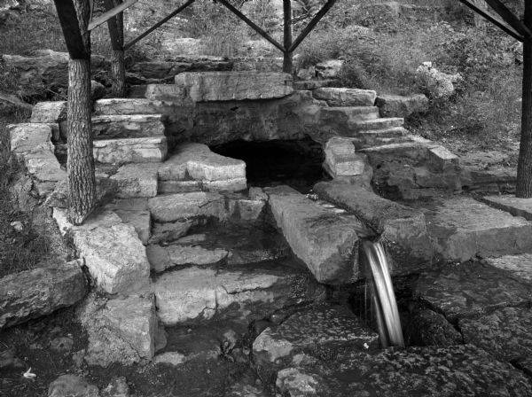 Close view of Lithia Spring which is built-up with stones and has tree trunks as a base for an (out of frame) roof overhead.