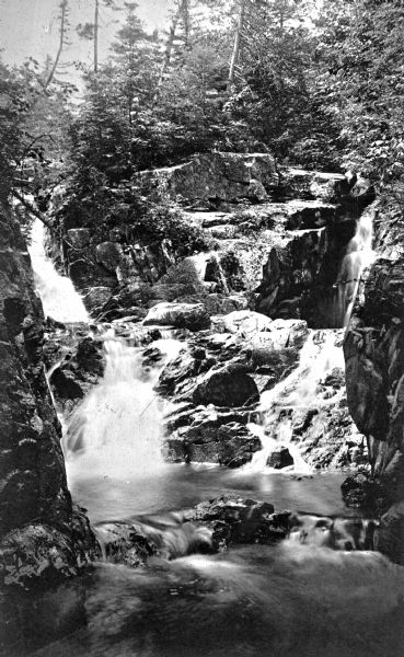 View of Beecher's Cascade, featuring water falling over the steep rocky hillside and pooling below. Trees are at the top of the cascade.