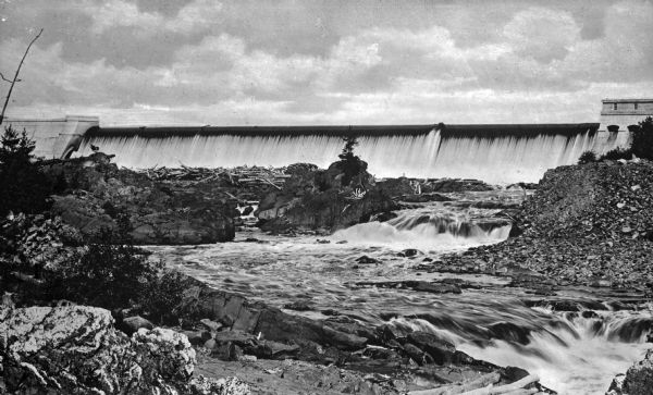 A downriver view of Great Northern Electric Company's Thompson Dam. In the foreground are rocky shallow falls.