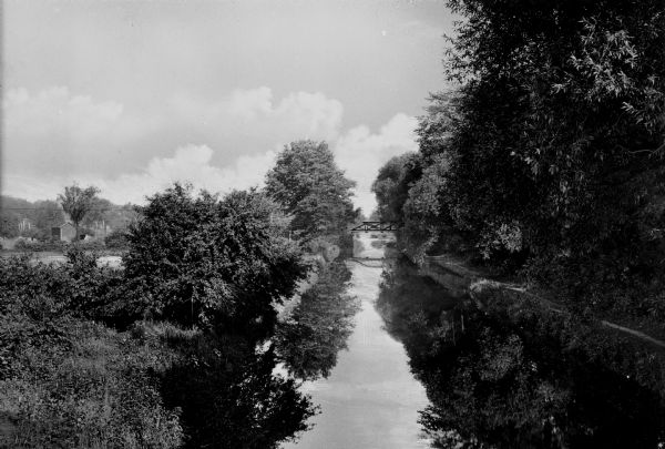 A view down the tree and bush lined Morris Canal with a steel bridge spanning the canal in the background.