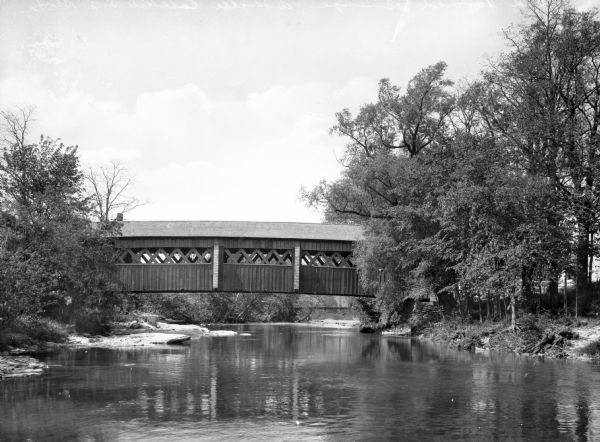View over water of a covered bridge with latticework windows.