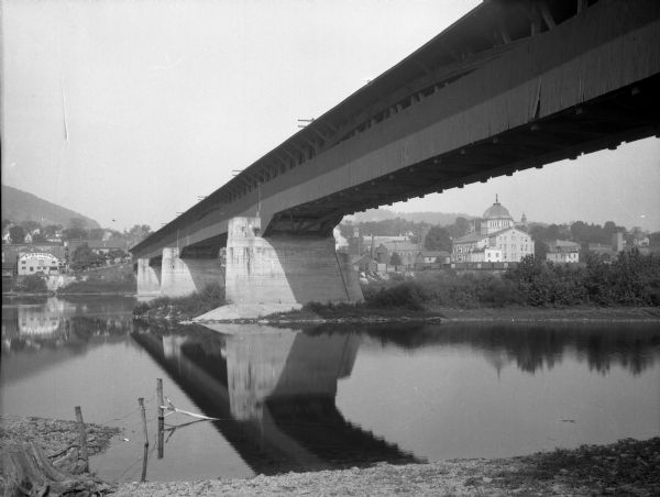 View from shoreline of a covered bridge over the Susquehannah River, with the Bradford county courthouse and other town buildings visible on the opposite shore.