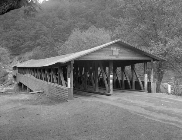 View of a two-lane covered bridge from one entrance.  Trees cover the steep hillside in the background.