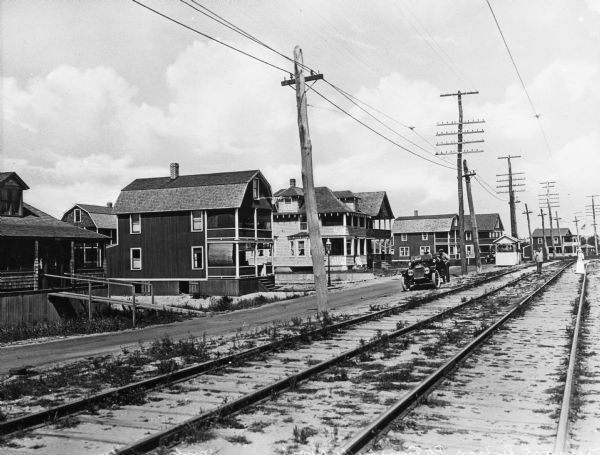 Tremont Railway Station showing traintracks, large houses on the bordering street, a car in the roadway and a small booth in the distance.