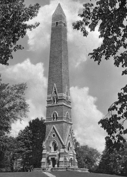 Ground level view of the Saratoga Monument, a brick obelisk framed by trees.