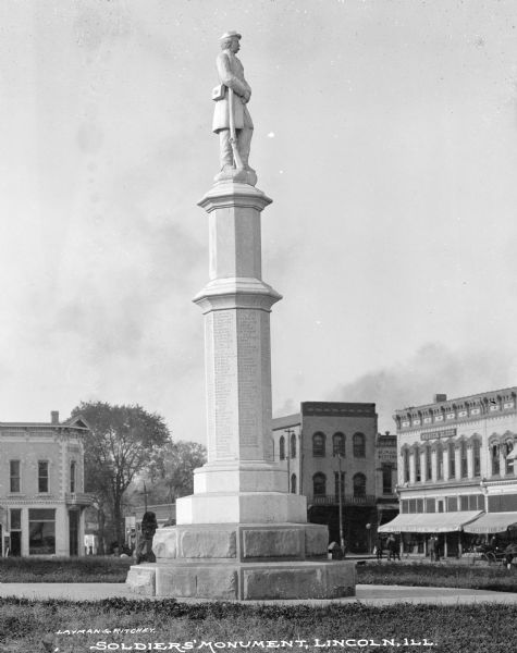 Originally published by Layman & Ritchey, this image features a marble soldier's monument dedicated to those who served in the Civil War, erected in 1869.  The monument is an inscribed octagonal column with a statue of a soldier at the summit.  Large town buildings are visible in the background.