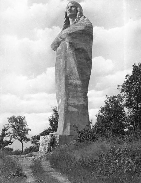 Sculpted by Lorado Taft, and dedicated in 1911, this statue of a Native American man wrapped in a blanket stands 48 feet tall and was originally named "The Eternal Indian."  Later, the statue was dubbed Chief Black Hawk by the locals.  The statue is located in a park and a man is leaning on the statue's pedestal.