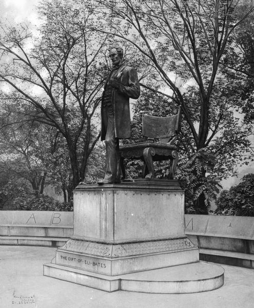 Augustus Saint-Gaudens' monument to Abraham Lincoln, installed 1887.  Image shows the bronze sculpture from its foot framed by young foliage in the background.