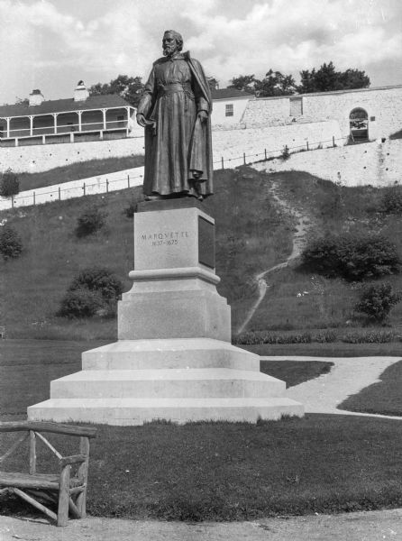 Close-up of a bronze statue honoring the French Jesuit missionary priest, Father Jacques Marquette in the park named after him. Unveiled in 1909 the statue stands at the bottom of a steep hill and the Officer's Stone Quarters at Fort Mackinac are visible at the summit of the hill.