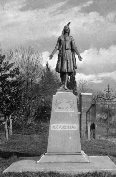 Close-up of a statue of Pocahontas located in the oldtown area of the city.  Installed in 1922, and sculpted by William Ordway Partridge, the bronze statue stands on a simple stone pedestal and trees and an ornate gate are visible in the background.