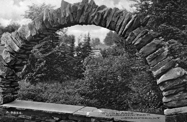 Close-up of a rough stone arch in Churchill Park. Greenery of the park is is visible through the arch.