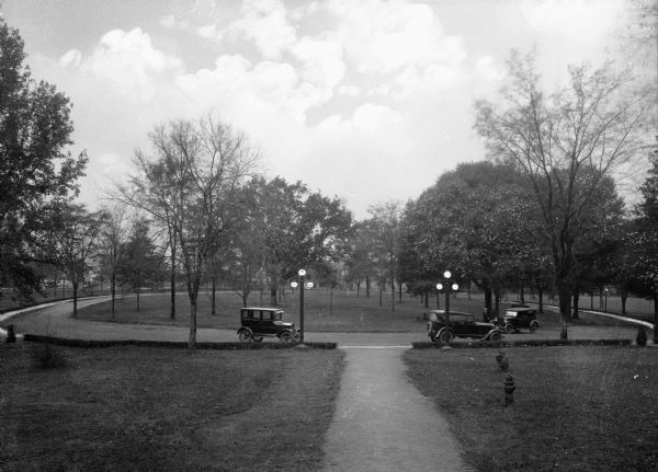 Cars parked in the circular drive on the campus grounds at Bessie Tift College.  The tree dotted lawn extends in all directions.
