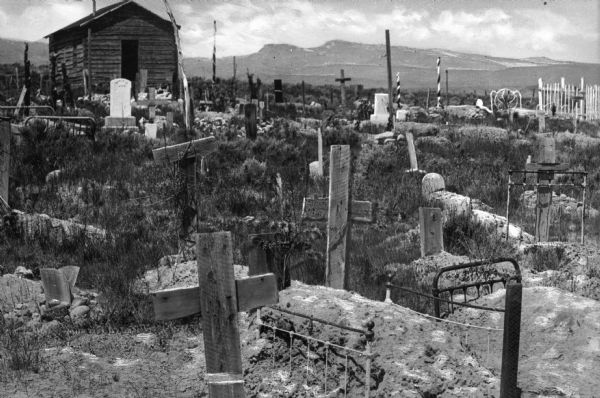 A view of a cemetery with wooden crosses and bedsteads used as fences.