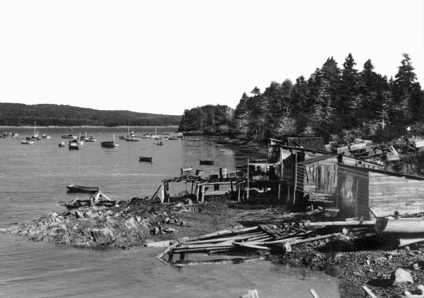 Elevated view of fishing boats moored in the harbor, with shacks along the shoreline in the foreground.