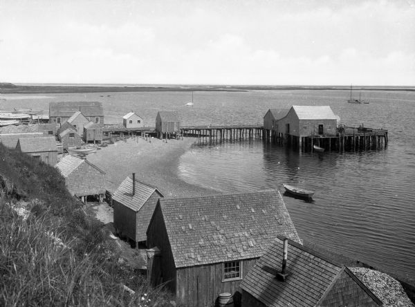 Elevated view from hill of a harbor with docks and shacks along the shoreline.