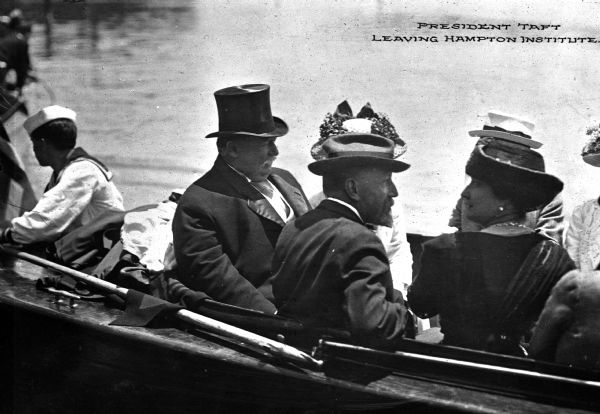 William Howard Taft (S9/15/1857 – 3/8/1930), the 27th President of the United States (3/4/1909 – 3/4/1913), wearing a top hat and sitting in a boat with a group of people as he leaves Hampton Institute, later to be known as Hampton University, in Hampton, Virginia. Caption reads: "President Taft Leaving Hampton Institute."