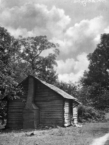 The birthplace of the Martha Berry School for girls, founded by Martha McChesney Berry (10/7/1865 – 2/27/1942). The school for girls would eventually evolve into Berry College in Rome, Georgia. There is a woman and child sitting in the open doorway on the side of the small log cabin.