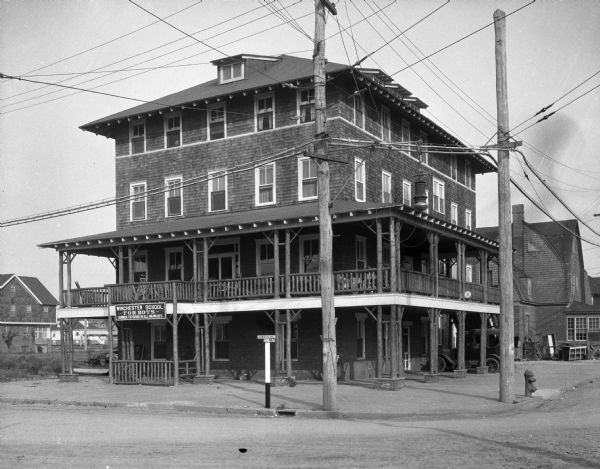 View from intersection toward the Winchester School for Boys, a four-story building, with the second floor featuring a wrap-around porch. The school is located on a street corner, with street signs that read: "Oberon Ave." and "24th Avenue."