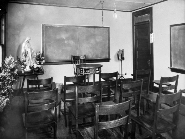 Interior view from the back of a classroom in the Academy of Jesus and Mary, including desks, chalkboards, and a large statue of the Virgin Mary.