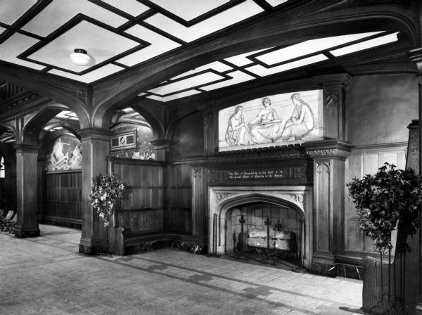 View of the foyer of Washington Irving High School, featuring a large fireplace, designed by the architect C.B.J. Snyder (1860-1945) and built in 1913 There are friezes or murals above the fireplace and woodwork around the room. Above the fireplace is engraved the words: "The Fire of Hospitality in the Hall, The genial Flame of Charity in the Heart."