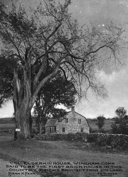 View of the Elderkin House with a stone wall in front. Caption reads: "Col. Elderkin House, Windham, Conn said to be the first brick house in the country, bricks brought from Holland. Hiram N. Fenn"