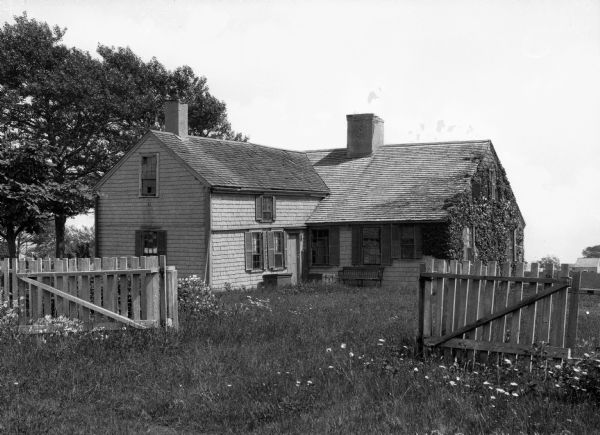 A view of a small Cape Cod home in a rural setting.
