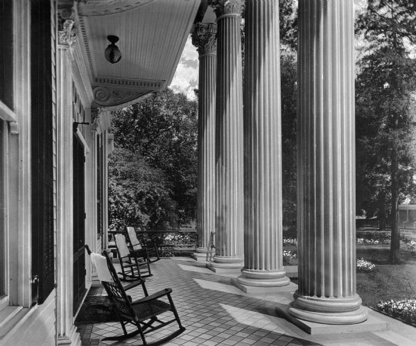 Rocking chairs, Corinthian columns, and decorative corbels are in this porch view of the residence of Richard Dhee.