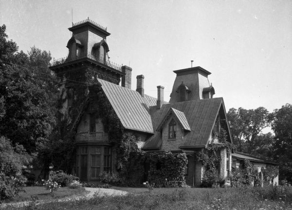 A view of an elaborate, ivy-covered country home with a tower.