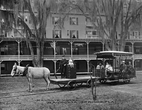 A horse-drawn vehicle on tracks delivering guests and their luggage at Magnolia Hotel. Caption reads: "Manolia[sic] Hotel, Magnolia, Springs, FLA."
