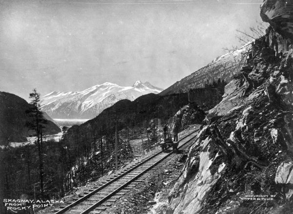 Two men pumping handcar on White Pass & Yukon Route Railroad.  This railroad served the needs of Yukon's population as well as its mining industry since 1898. Today it is designated an International Historic Civil Engineering Landmark.