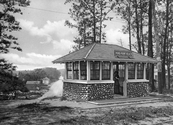 A woman waiting inside Pond Point Beach's railway station. Beyond the station, there are beach houses and the waterfront.
