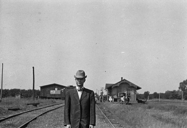 View of a man wearing a hat and suit standing in the foreground, with the Sterling depot in the background. The depot is a stop on the Atchison, Topeka, and Santa Fe Railroad, constructed between August 1909 and 1910.