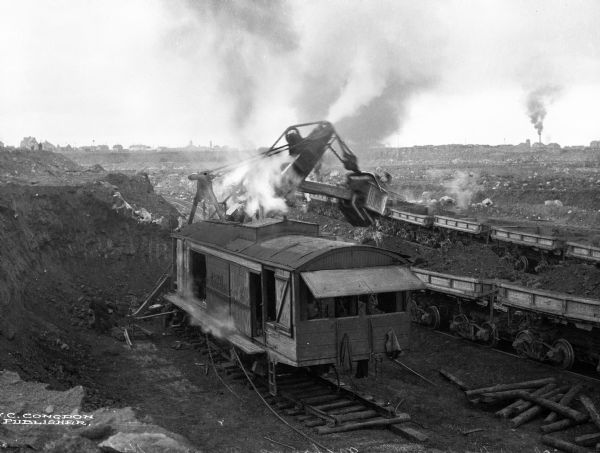 A steam shovel loading ore at the Hull Rust Mahoning Mine, the world's largest open pit iron ore mine. Published by J.C. Congdon.