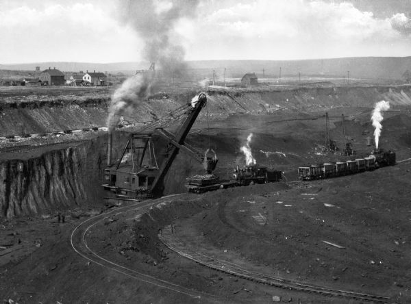 Miners at work using steam shovels and railroad cars for transporting iron ore in Virginia, located on the Mesabi Iron Range.