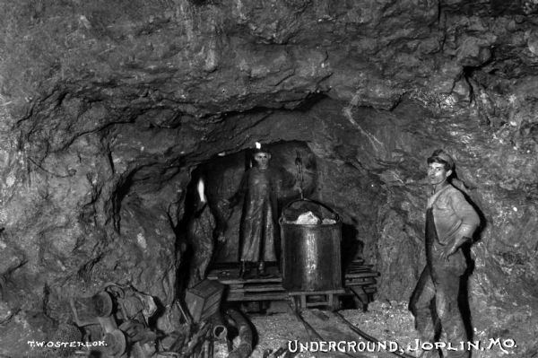 Two miners in the interior of a mine. Soon after the turn of the century, Joplin was named the lead and zinc capital of the world. Caption reads: "Underground, Joplin, MO."