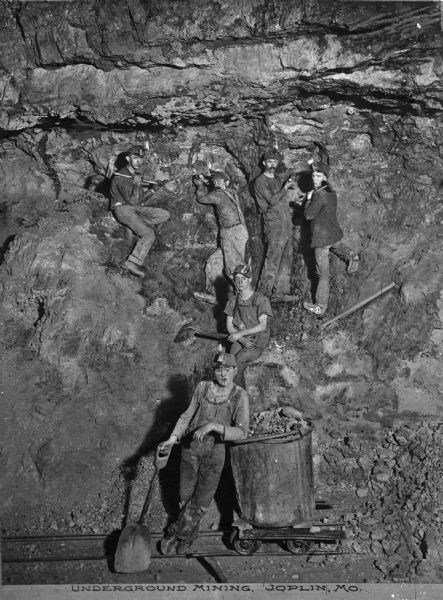 Soon after the turn of the century, Joplin was named the lead and zinc capital of the world. A group of young men are shown mining underground. Caption reads: "Underground Mining, Joplin, MO."